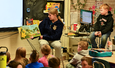 High school student reads a book to an elementary school classroom