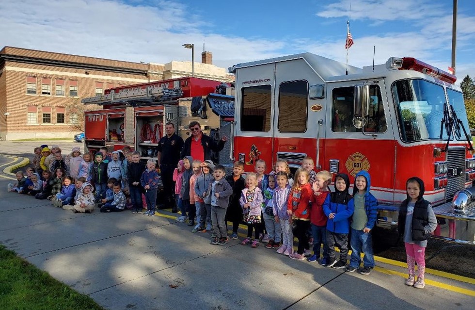 Pre-K students smiling with firefighters next to a firetruck