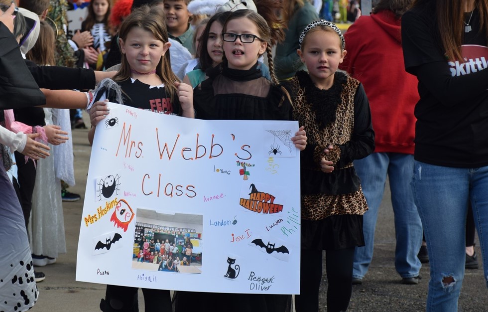 students walking in the halloween parade holding a sign with their teachers name on it
