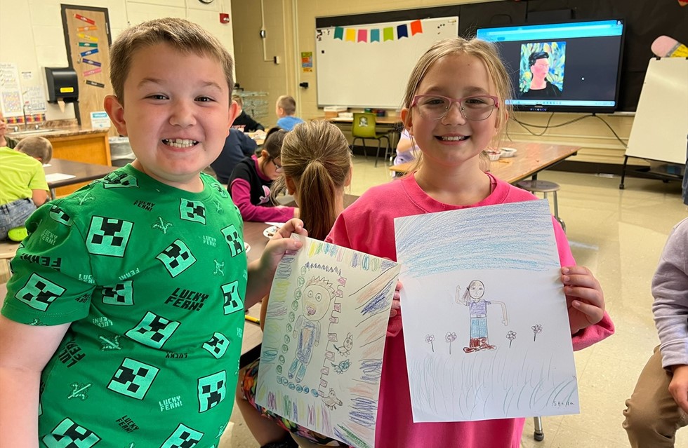 Students hold up their artwork in a classroom